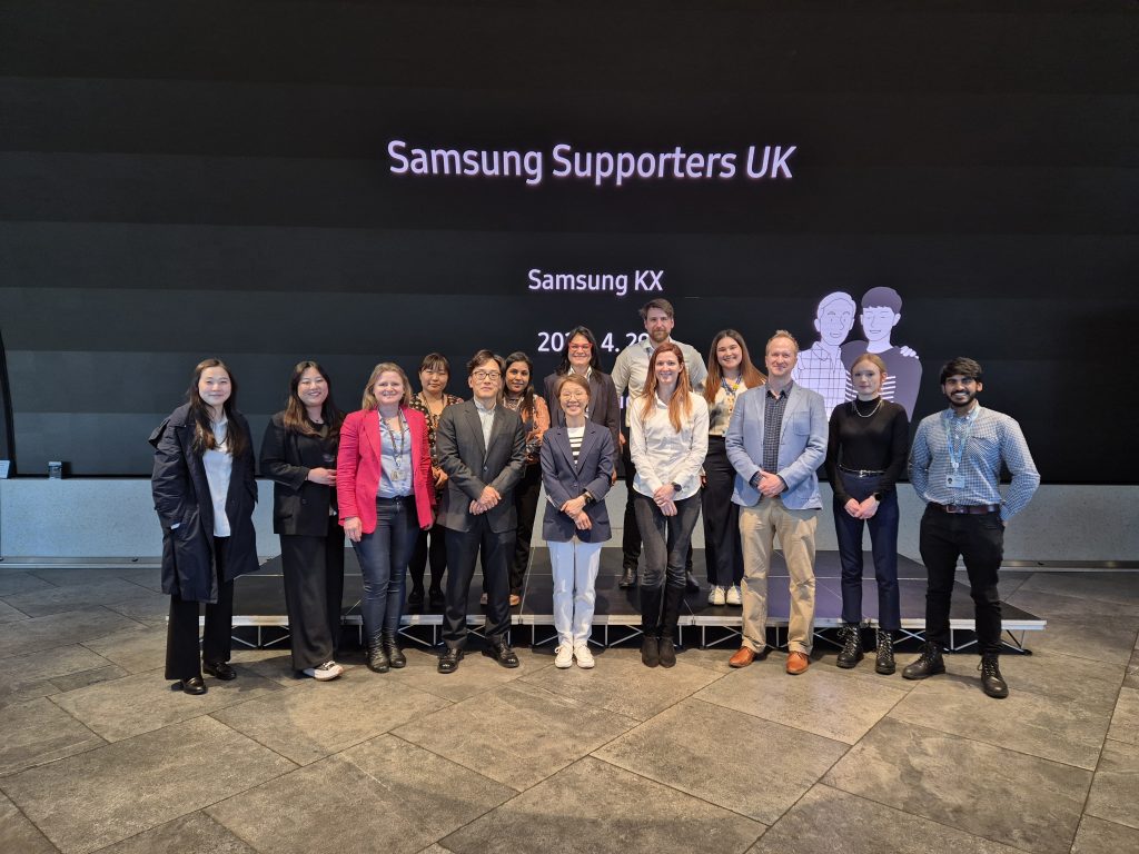 'Image of 14 Samsung colleagues including VP Jeong-sook Lee (VP of Experience Planning Group, MX Business, Samsung UK) smiling and standing together on the Samsung KX stage for the Samsung Supporters event